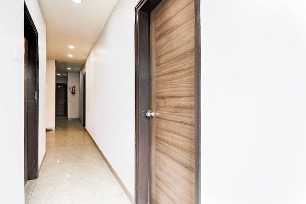 Un pasillo con una puerta de madera a la derecha, un extintor en la pared y otra puerta al final.