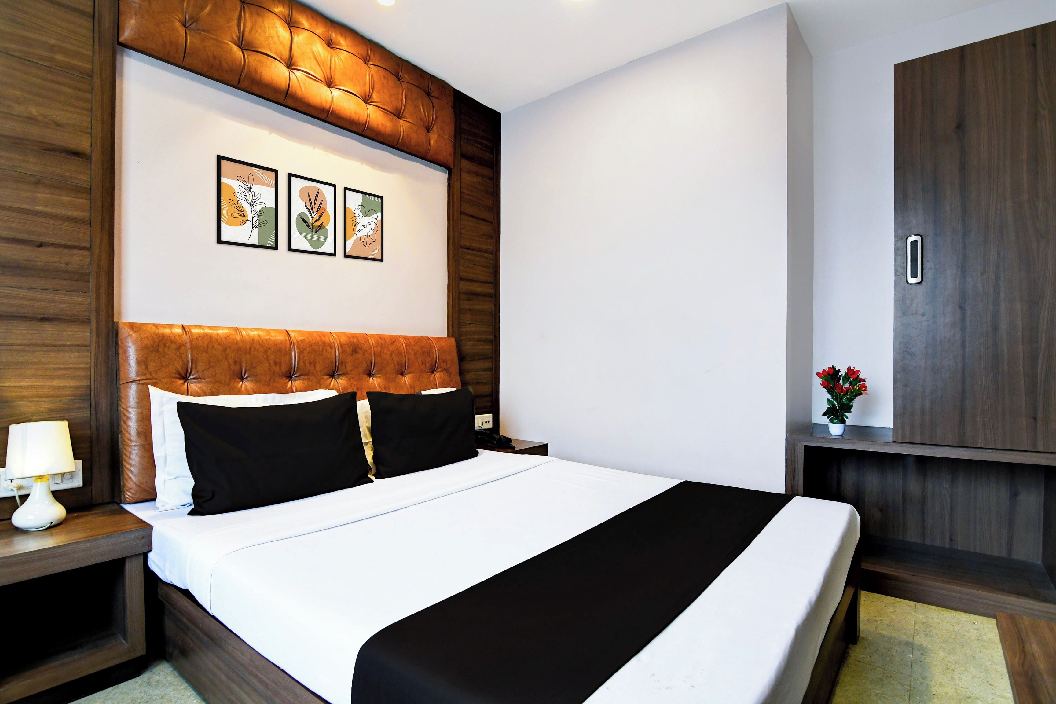 A hotel room with a large bed, a wooden headboard, a nightstand, a lamp, and a small table with a plant.