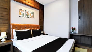 A hotel room with a large bed, a wooden headboard, a nightstand, a lamp, and a small table with a plant.