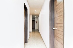 A corridor with a wooden door on the right and a fire extinguisher mounted on the wall. - Super Hotel O Tagore Park Laskarhat (Kolkata)