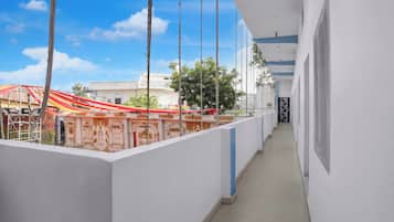 A corridor with a view of a building with a red roof and scaffolding, a white wall with a blue stripe, and a door with a black and white design.