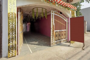 An open gate with intricate metalwork, leading to a building with a pink wall and a decorative archway.