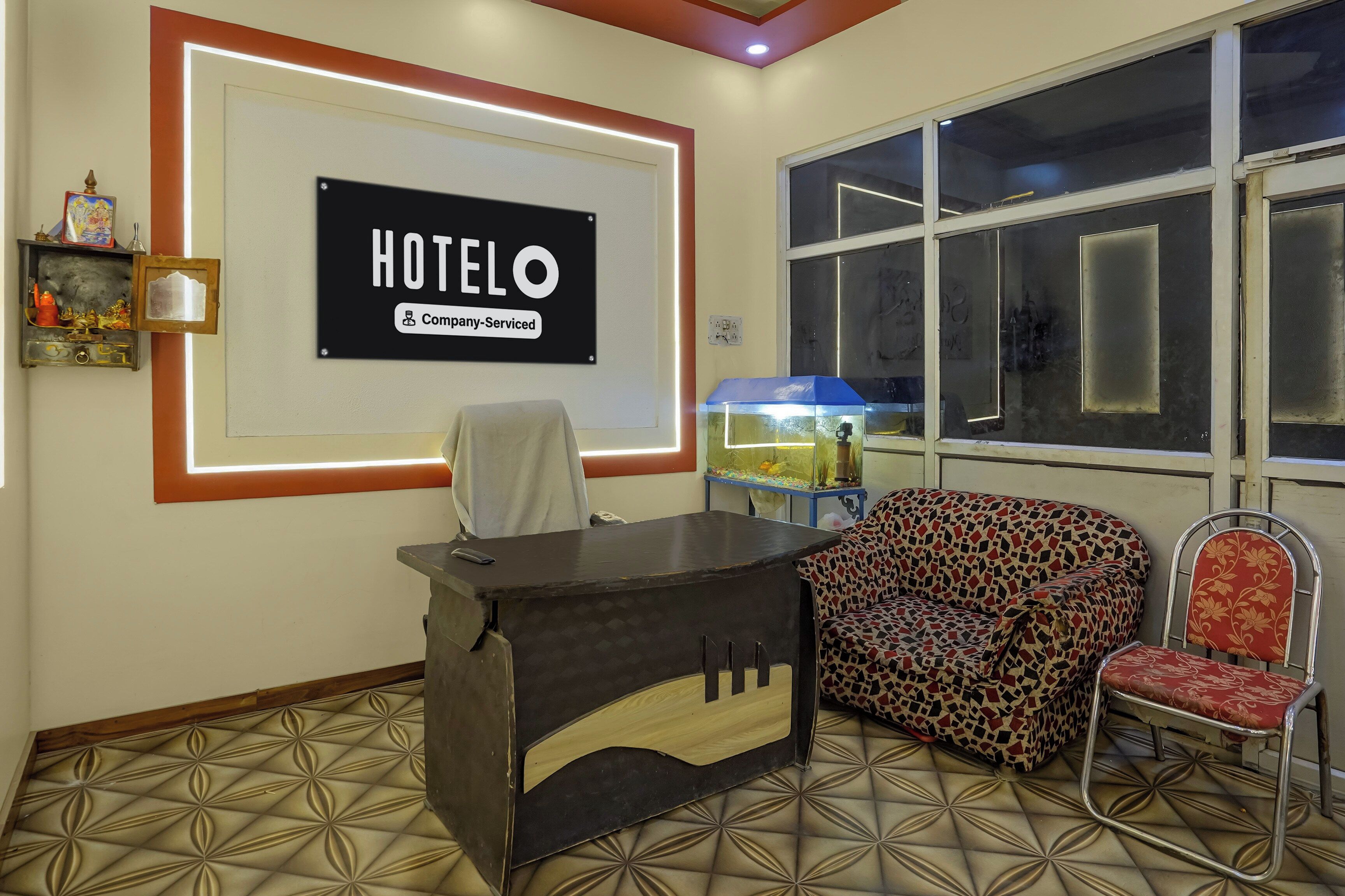 A hotel reception area with a reception desk, a sofa, and a chair. There is a large sign on the wall that reads 'HOTELO Company-Serviced'.