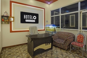 Zona de recepción de un hotel con mostrador, un sofá y una silla. Un letrero grande en la pared dice 'HOTELO Company-Serviced'.