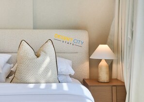 Una habitación de hotel con cama, almohadas, una mesita de noche y una lámpara.