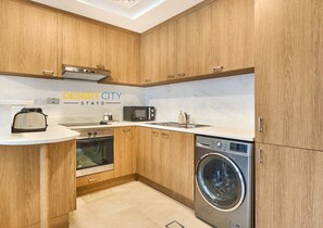 A compact kitchen with wooden cabinets, a microwave, an oven, a dishwasher, and a toaster. - Chic & Stylish Unit|Prime Location Near Dubai Mall (Dubai)