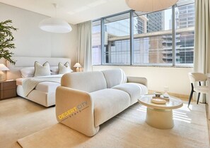 A modern hotel room with a sofa, a round coffee table, and a view of the cityscape through large windows. - Chic & Stylish Unit|Prime Location Near Dubai Mall (Dubai)