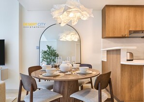 A modern dining area with a round table set for four, a large mirror, and a kitchen area with wooden cabinets. - Chic & Stylish Unit|Prime Location Near Dubai Mall (Dubai)