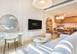 A modern living room with a flat-screen TV, a round mirror, a sofa, and a dining area with wooden cabinets and chairs. - Chic & Stylish Unit|Prime Location Near Dubai Mall (Dubai)
