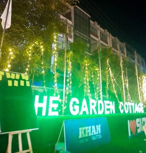 A sign for 'HE GARDEN COTTAGE' with decorative lights and a sign for 'KHAN' below it.