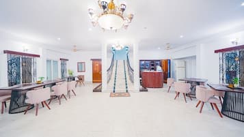 Un amplio vestíbulo de hotel con una imponente araña, una escalera central y un área de comedor con mobiliario moderno.