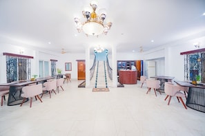 A spacious hotel lobby with a grand chandelier, a central staircase, and a dining area with modern furniture.
