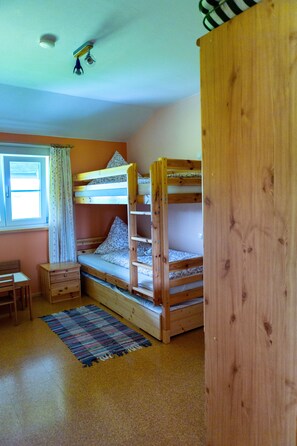 Ein Schlafraum mit Etagenbett, Fenster, Schreibtisch und einem gemusterten Teppich.