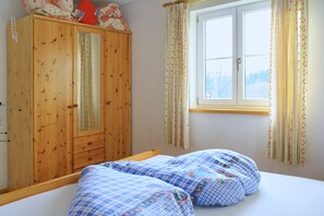 Ein Schlafzimmer mit einem Holzschrank, einem Bett mit floralem Bettzeug und einem Fenster mit Vorhängen.