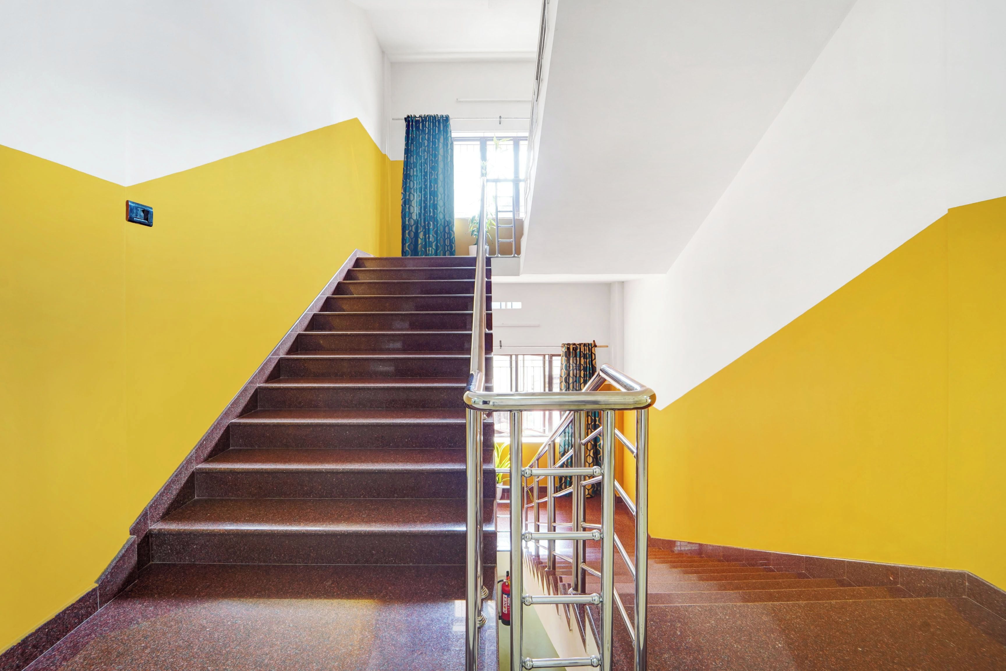 Una escalera con barandilla de metal que lleva a un rellano con una ventana y una cortina azul.
