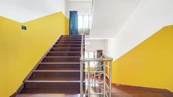 Una escalera con barandilla de metal que lleva a un rellano con una ventana y una cortina azul.