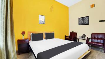 Habitación de hotel con una cama grande, una mesita de noche, una silla y una pequeña mesa con una tetera.