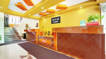 A hotel reception area with a reception desk, a staircase, and a sign indicating 'HOTEL' and 'BOOKING & SERVICE'.