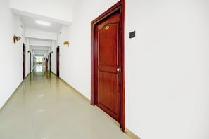 A long, narrow hallway with a wooden door on the right, white walls, and a tiled floor.