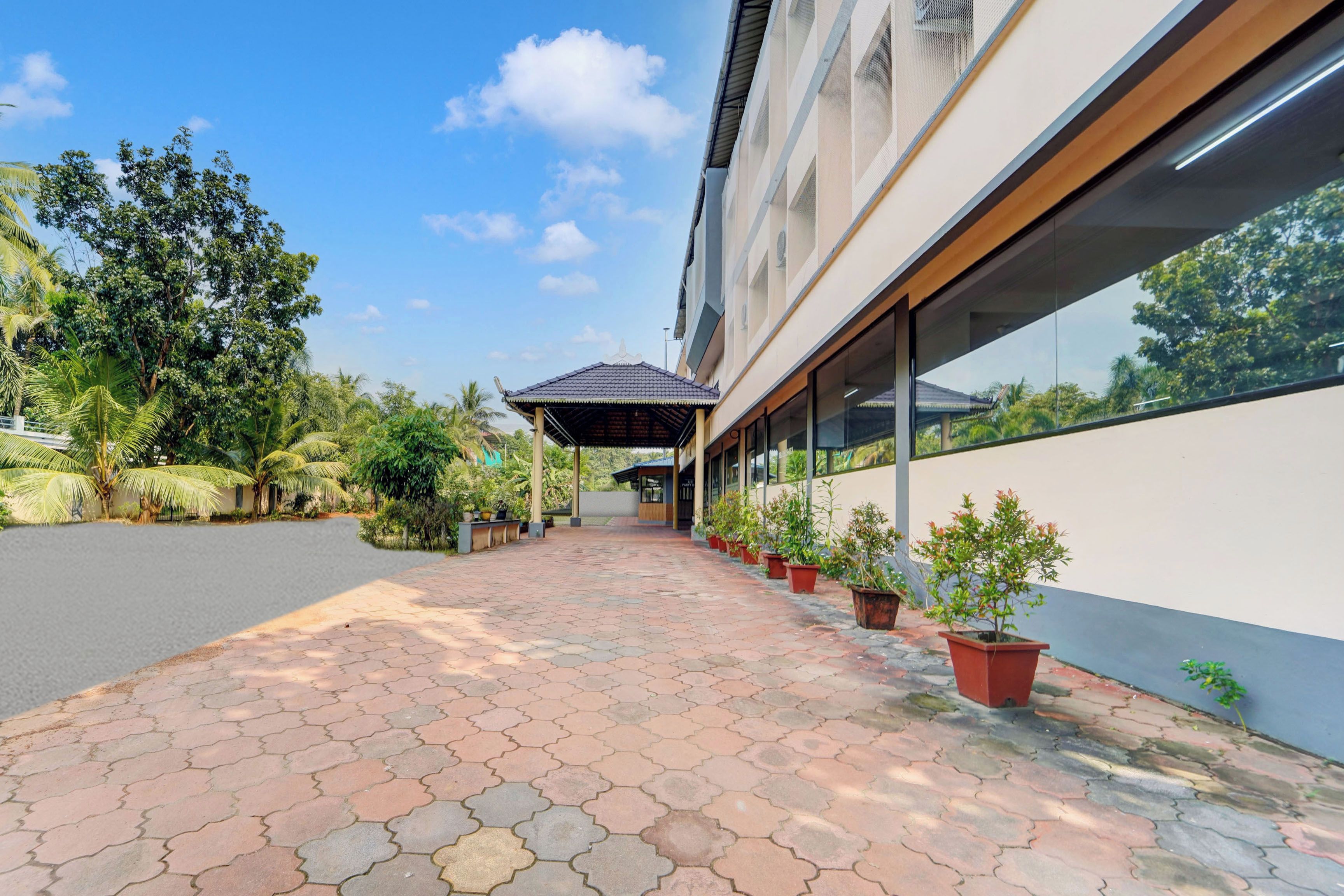 A pathway leading to a building with a covered entrance, surrounded by potted plants and trees.