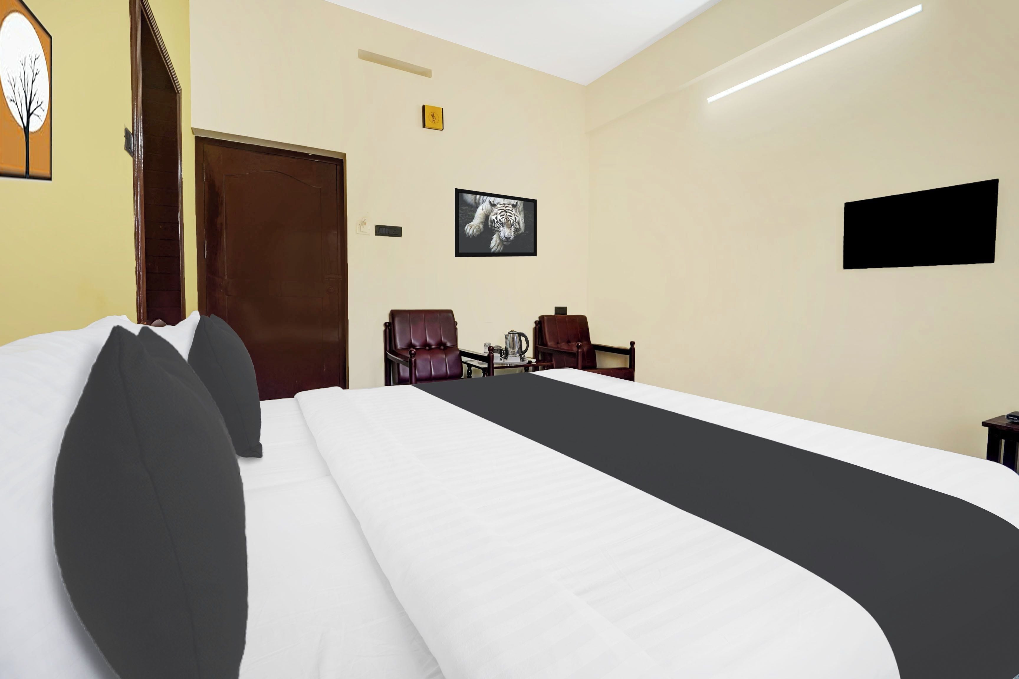 Quarto de hotel com uma cama grande, duas cadeiras, uma televisão de tela plana e uma porta.
