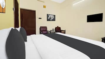 Quarto de hotel com uma cama grande, duas cadeiras, uma televisão de tela plana e uma porta.
