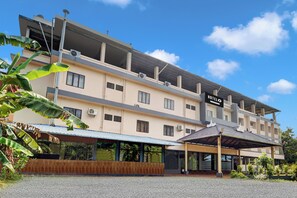 A multi-story hotel with a flat roof, large windows, and a covered outdoor seating area.