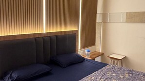 A hotel room with a bed, a nightstand, a lamp, and a window with blinds. - Room-charming B&B Room With Private Faci (Jammu)