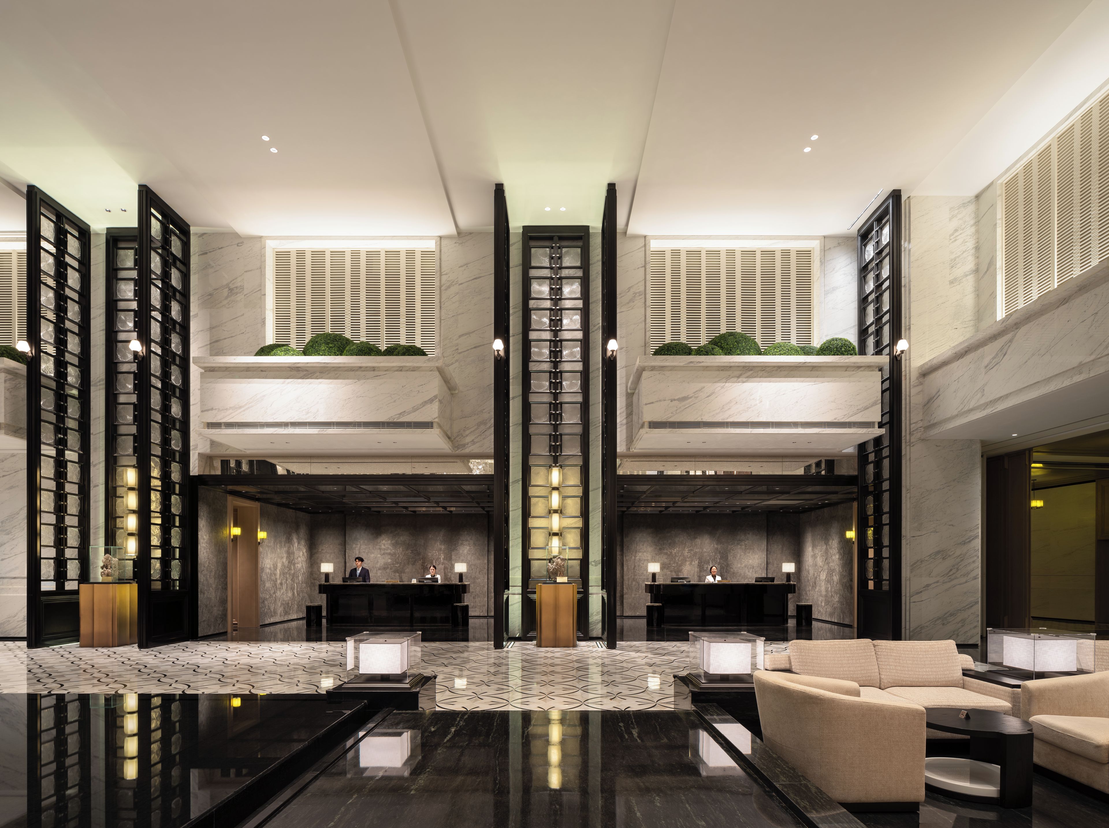 A modern hotel lobby with a reception desk, seating area, and a high ceiling with skylights.