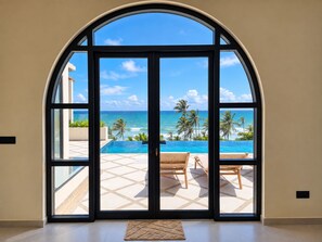 A room with a large arched glass door leading to a pool area with a view of the ocean and palm trees. - Thilo Villa Matara (Matara)