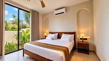 A hotel room with a large bed, two bedside tables with lamps, an air conditioning unit, and a view of greenery through a sliding door.