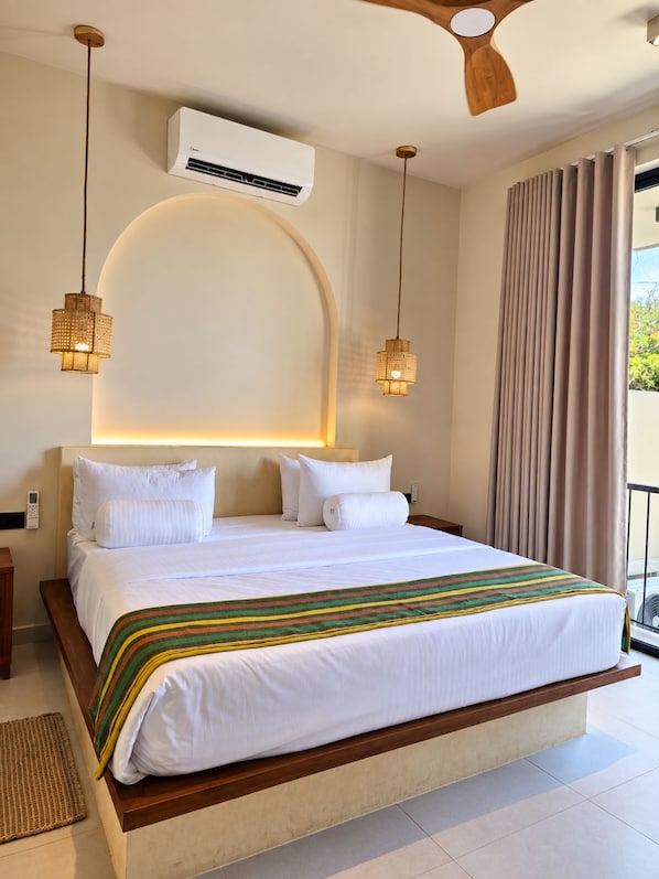 A hotel room with a large bed, two bedside lamps, an air conditioning unit, and a view of the outdoors.