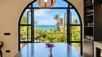A kitchen with a marble countertop, a vase with flowers, and a view of the ocean through large windows.