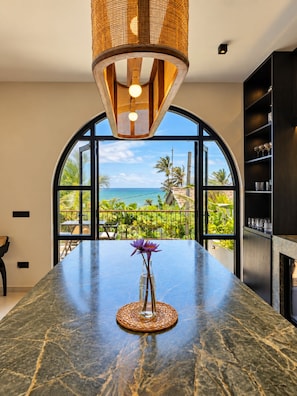 A kitchen with a marble countertop, a vase with flowers, and a view of the ocean through large windows.