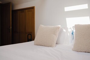 A bedroom with a wooden door, a white bed with fluffy pillows, and a window providing natural light. - Beautiful 4BD Cottage in Minchinhampton (Minchinhampton)