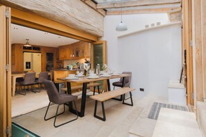 Een moderne keuken met houten kasten, een eethoek met een tafel en stoelen, en uitzicht op het buiten.