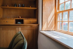 A wooden cabinet with drawers and shelves, a window with a view of the outside, and a cushion on a chair. - Beautiful 4BD Cottage in Minchinhampton (Minchinhampton)
