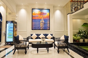 A lobby with a sofa set, a coffee table, a painting of a sailboat, and a vending machine.