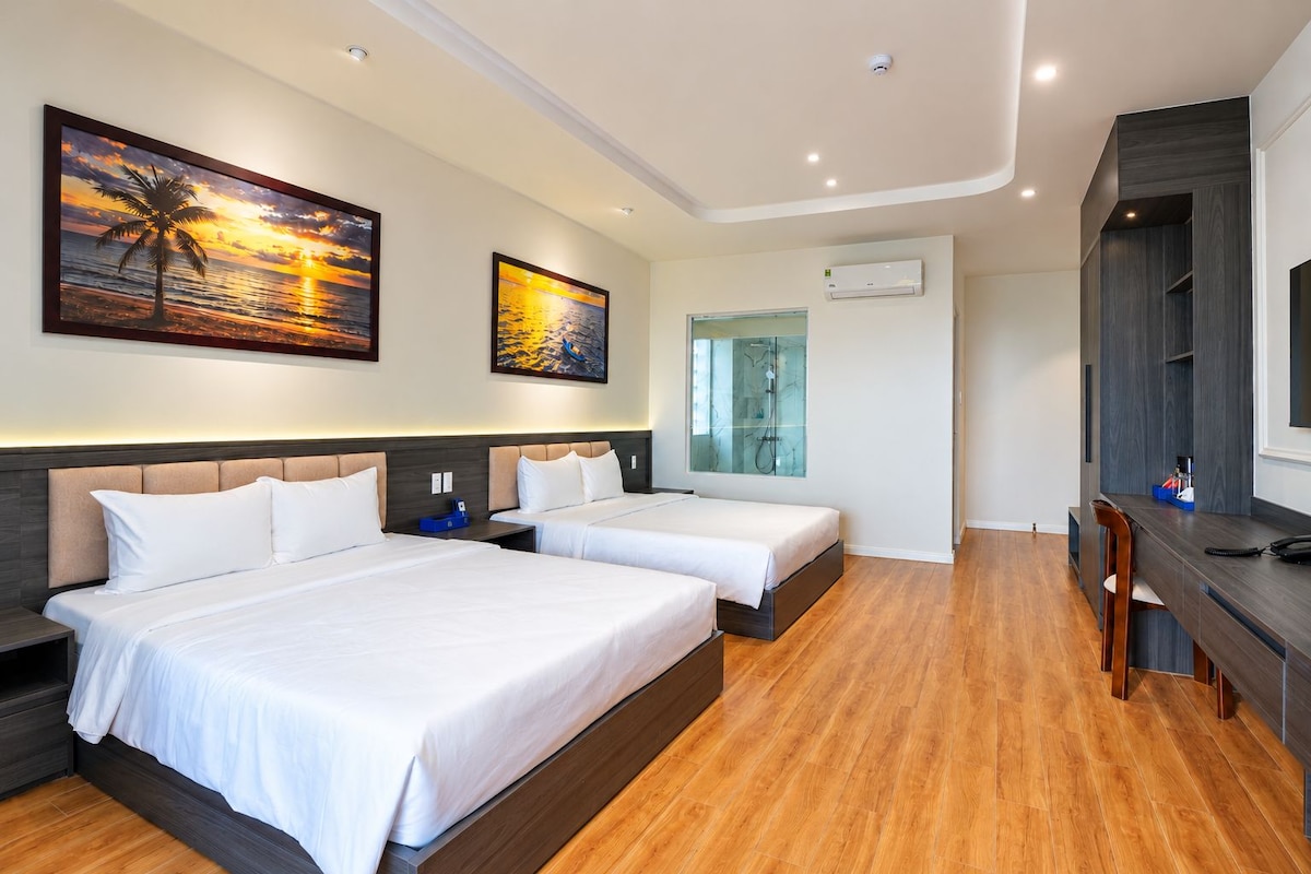 A hotel room with two beds, a desk, and a shower area.