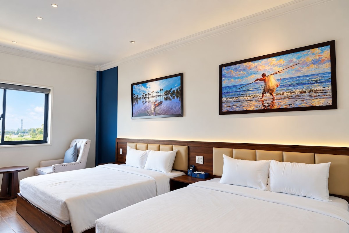 A hotel room with two beds, a chair, a nightstand, and artwork on the walls.
