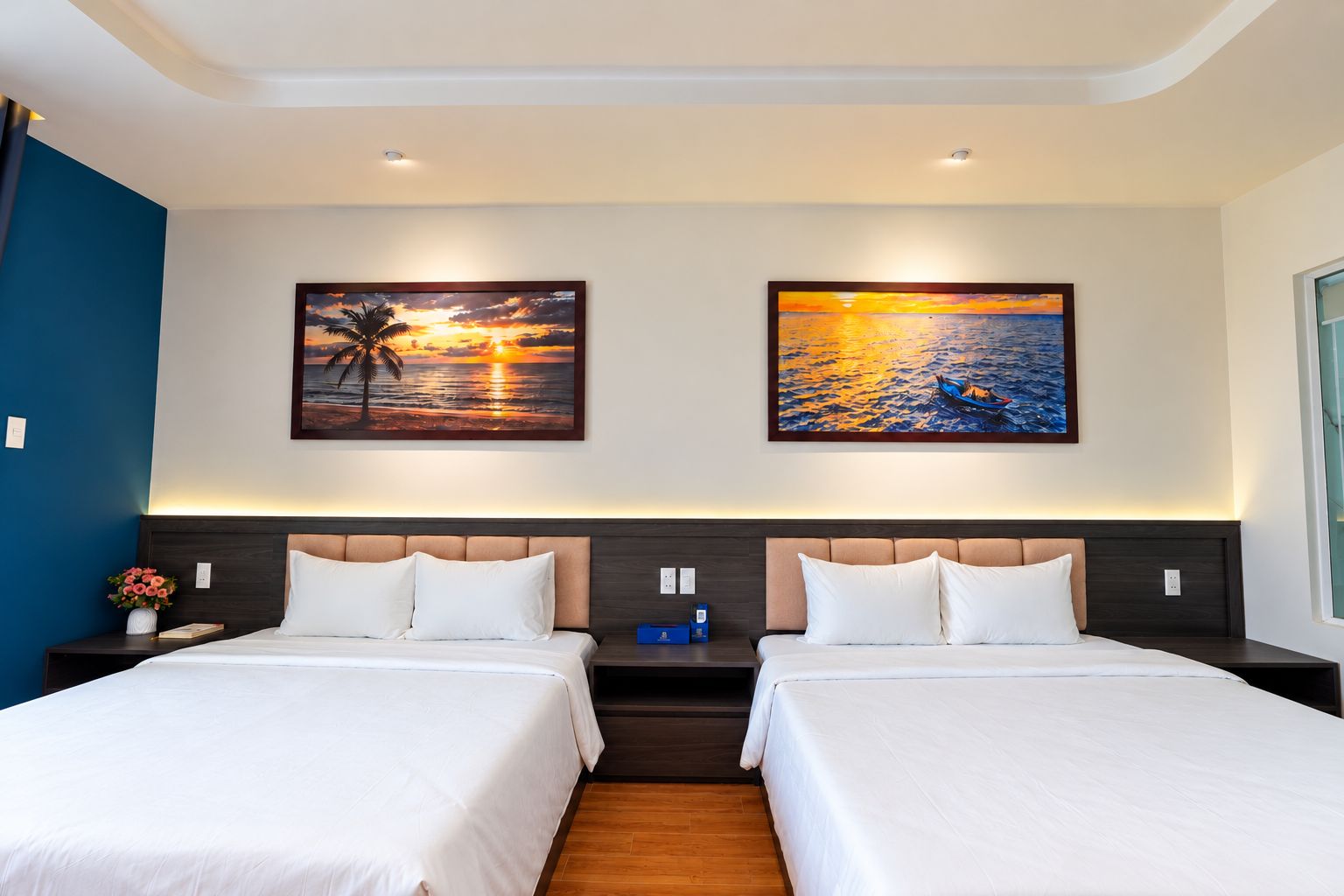 Ein Hotelzimmer mit zwei Betten, einem Nachttisch mit Blumenvase und zwei an der Wand hängenden Bildern.