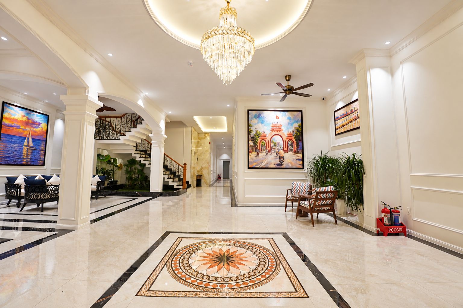 A hotel lobby with a grand chandelier, a large painting of a cityscape, a fire extinguisher, and a modern staircase.
