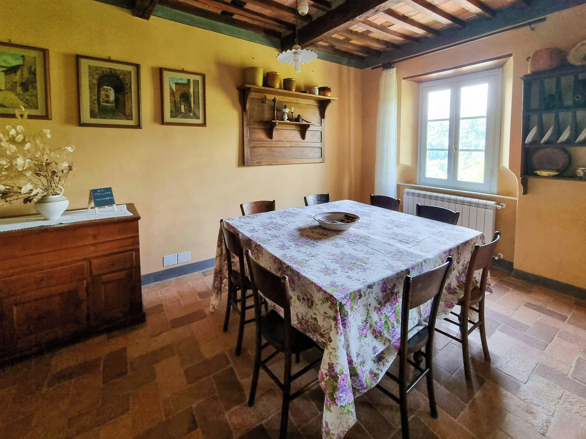 Ein Essbereich mit einem Tisch, gedeckt für vier Personen, flankiert von Stühlen, einem Holzschrank und einem Regal mit Küchenutensilien.
