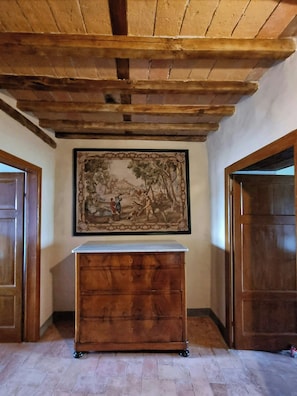 Ein Zimmer mit Holzboden, einem großen gerahmten Gemälde, einer hölzernen Kommode und zwei Holztüren.