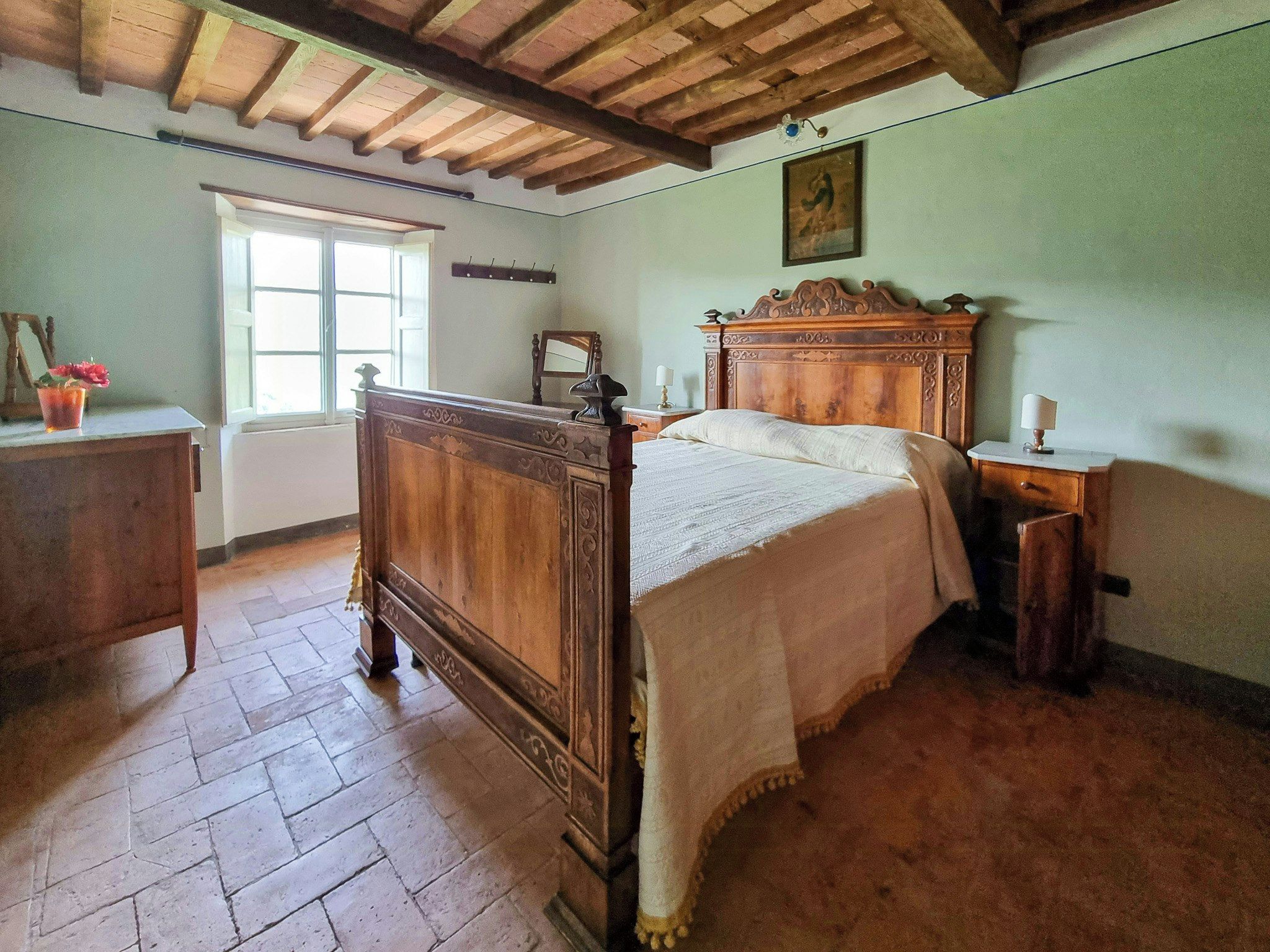 Una camera da letto tradizionale con un letto in legno, un comodino, tende a una finestra.