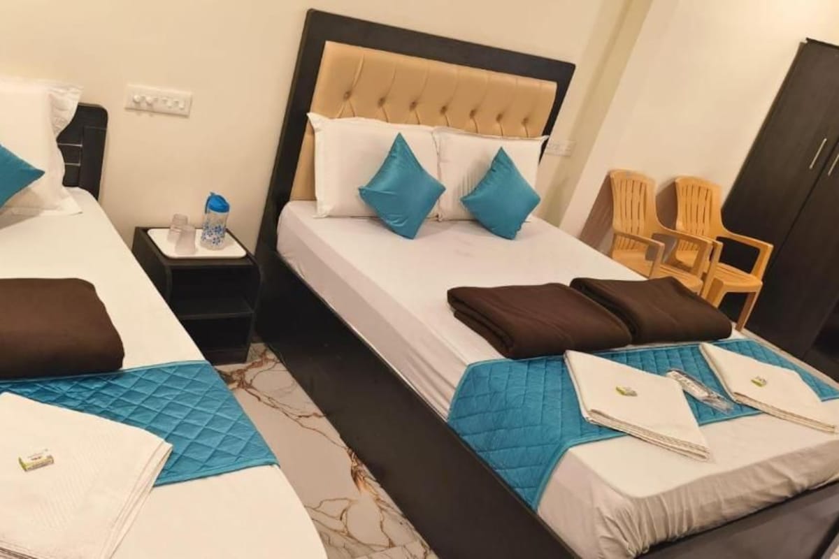 Habitación de hotel con dos camas, cada una con edredón, almohadas y colcha acolchada. Hay dos mesitas de noche con lámparas y una botella de agua.