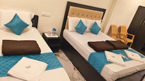 Habitación de hotel con dos camas, cada una con edredón, almohadas y colcha acolchada. Hay dos mesitas de noche con lámparas y una botella de agua.