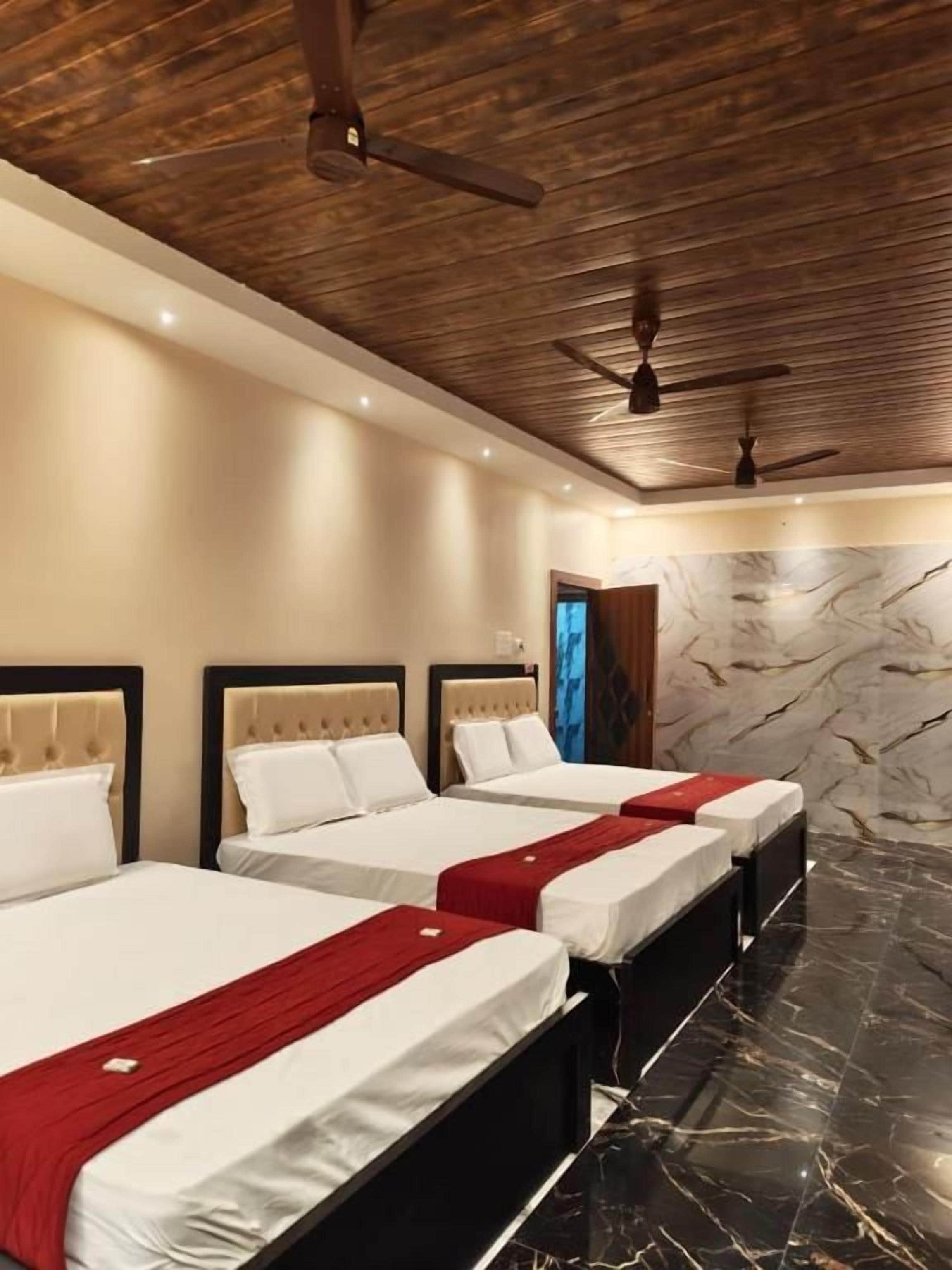 A hotel room with three beds, wooden ceiling, marble wall, and a red throw blanket.