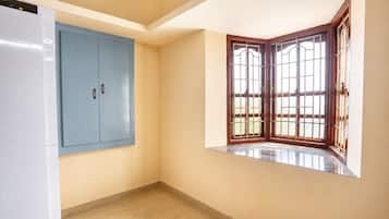 A room with a blue wardrobe, a corner window with wooden frames, and a white refrigerator.