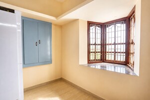 Una habitación con un armario azul, una ventana en esquina con marcos de madera y un refrigerador blanco.